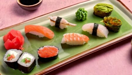 A platter displaying multiple types of sushi including nigiri, maki rolls, and gunkan maki served with wasabi, pickled ginger, and soy sauce