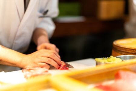 A sushi chef using a sashimi knife cut in a fresh fish on a cutting board during professional kitchen preparation