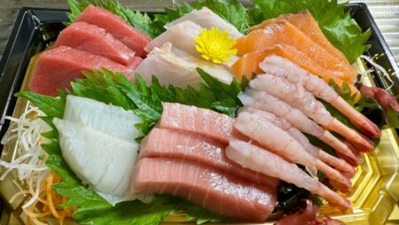 A premium sashimi platter featuring multiple sashimi cuts including tuna, salmon, flounder, toro, and shrimp served on shiso leaves