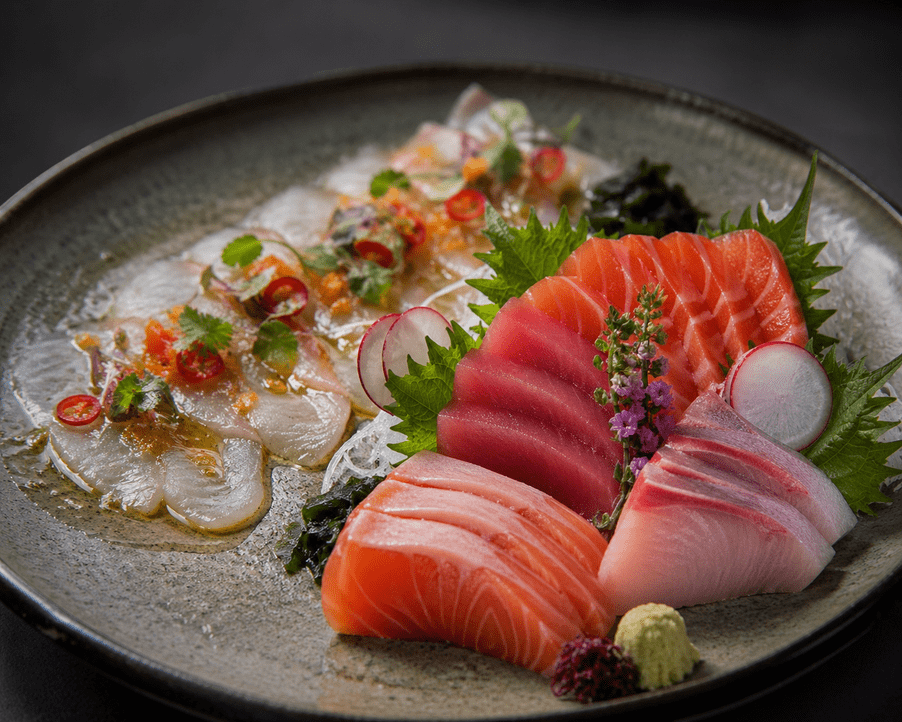 A composed plate showing sashimi vs crudo side by side featuring traditional sashimi cuts of tuna salmon and yellowtail alongside crudo-style white fish dressed with chili herbs and citrus