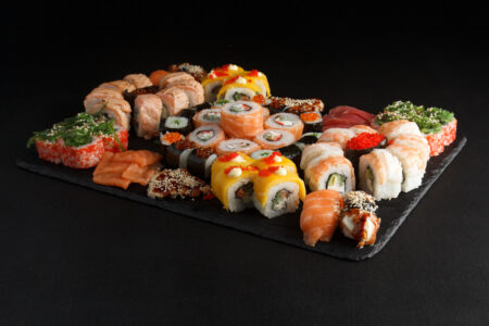 A large sushi pairing spread featuring multiple roll types including uramaki, specialty rolls with tobiko, and salmon rolls arranged on a dark slate board