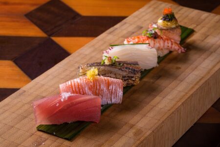 A precision-plated lineup by a skilled sushi chef featuring tuna sashimi salmon mackerel white fish king crab and gunkan maki arranged sequentially on a wooden board