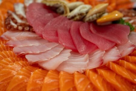 A seasonal sashimi menu platter featuring multiple fish cuts including tuna, salmon, yellowtail, and shellfish arranged together