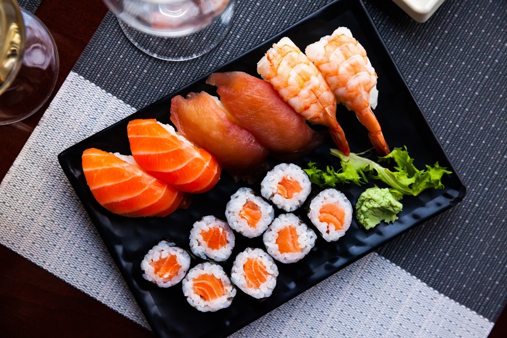 An overhead view of a mixed sushi texture plate featuring salmon sashimi slices tuna and shrimp nigiri and salmon hosomaki rolls served with wasabi on a black dish