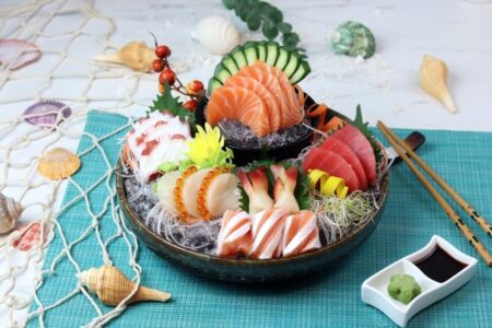 An assorted sashimi platter served on ice featuring the best fish for sashimi including salmon tuna scallop shrimp white fish and squid arranged in a ceramic bowl with soy sauce and wasabi