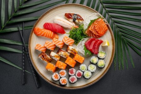 Overhead view showing the difference between sashimi and sushi on one ceramic plate featuring salmon and tuna sashimi slices nigiri maki rolls and specialty rolls with seaweed salad and chopsticks
