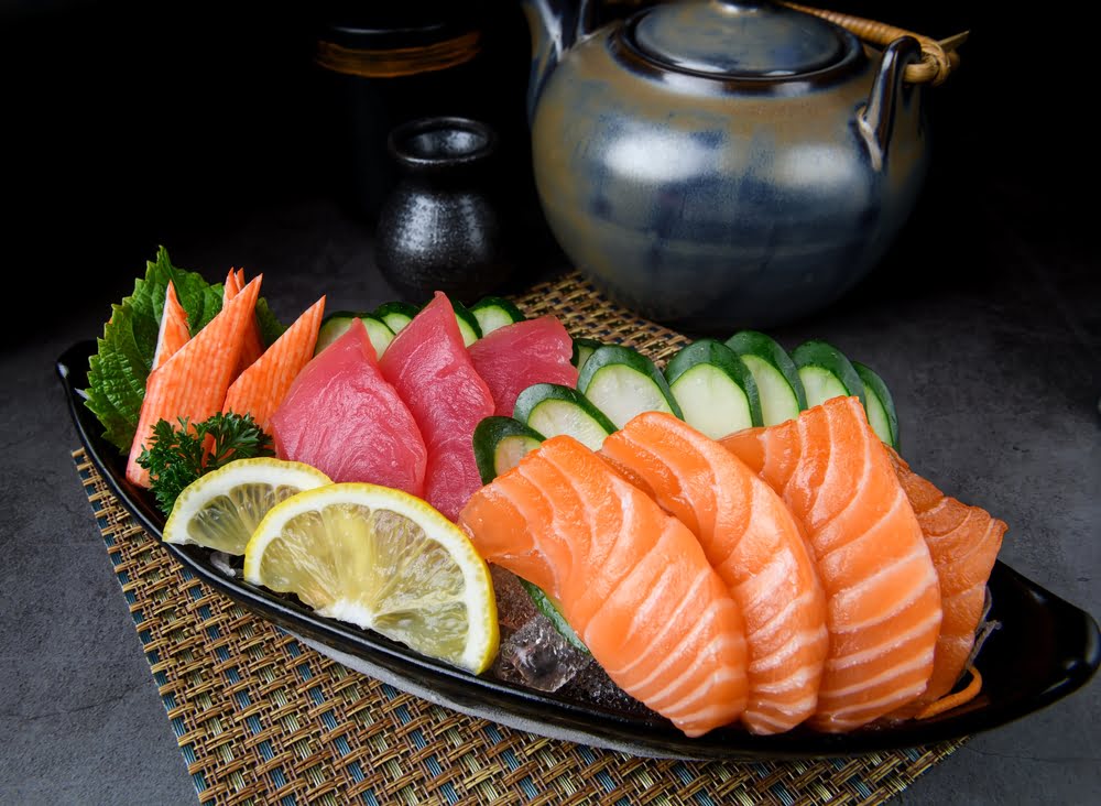 Fresh sashimi in Homecrest Brooklyn featuring a platter of sliced salmon, tuna, and cucumber garnished with lemon wedges parsley and shiso leaves served at Masuta Japanese Fusion Restaurant