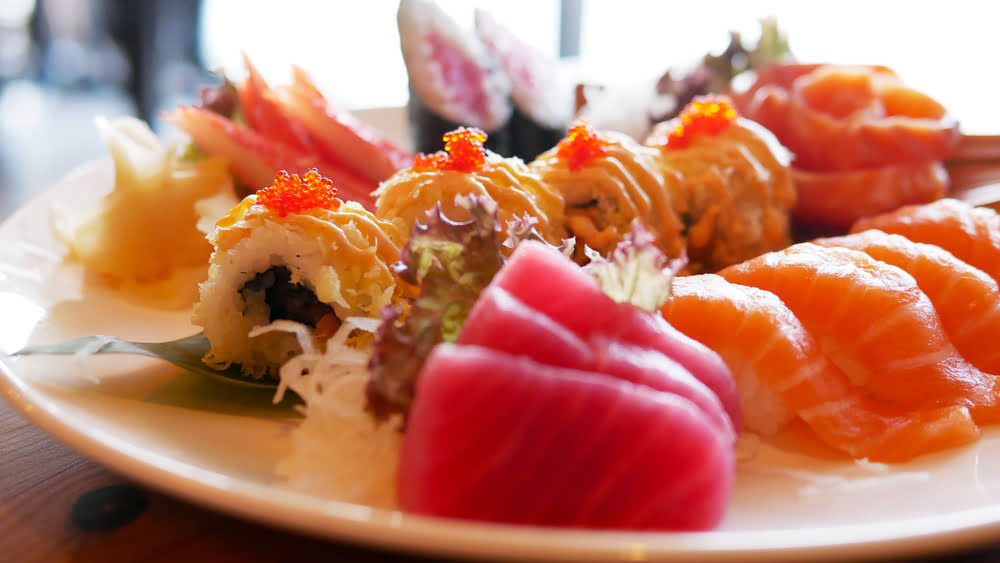 A combined plate showing both sushi or sashimi options featuring thick-cut tuna and salmon sashimi slices alongside tobiko-topped specialty sushi rolls with pickled ginger on a round ceramic plate