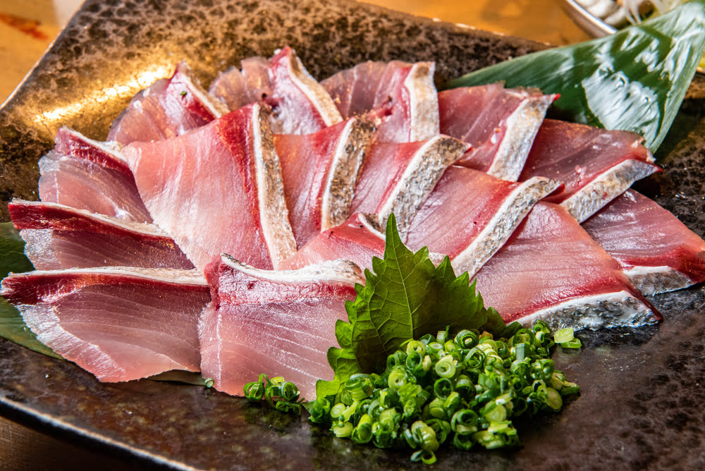 Fresh yellowtail sashimi in Midwood Brooklyn fanned across a dark stone plate garnished with shiso leaf and sliced green onion served at Masuta Japanese Fusion Restaurant